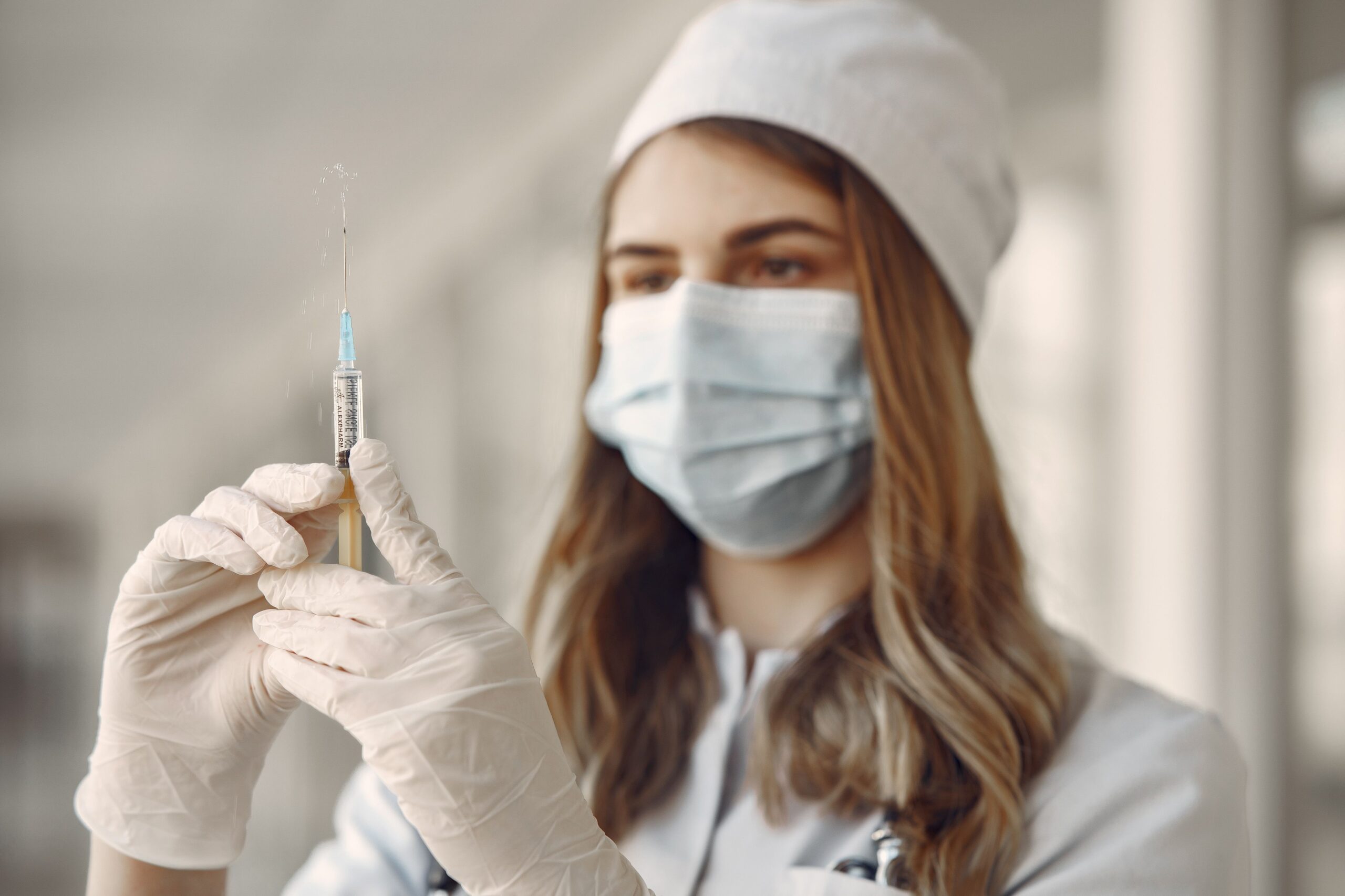 A female doctor in a face mask fills a syringe with vaccine indoors, emphasizing healthcare and safety.